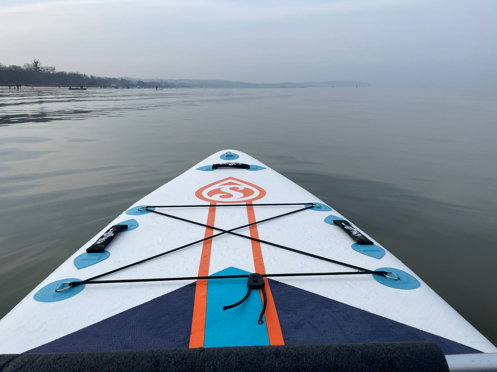 Widok z deski SUP na spokojną wodę i linię brzegu